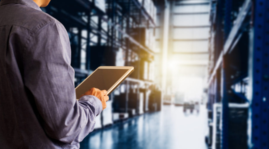 A business professional using a tablet in a large warehouse-warehouse management system