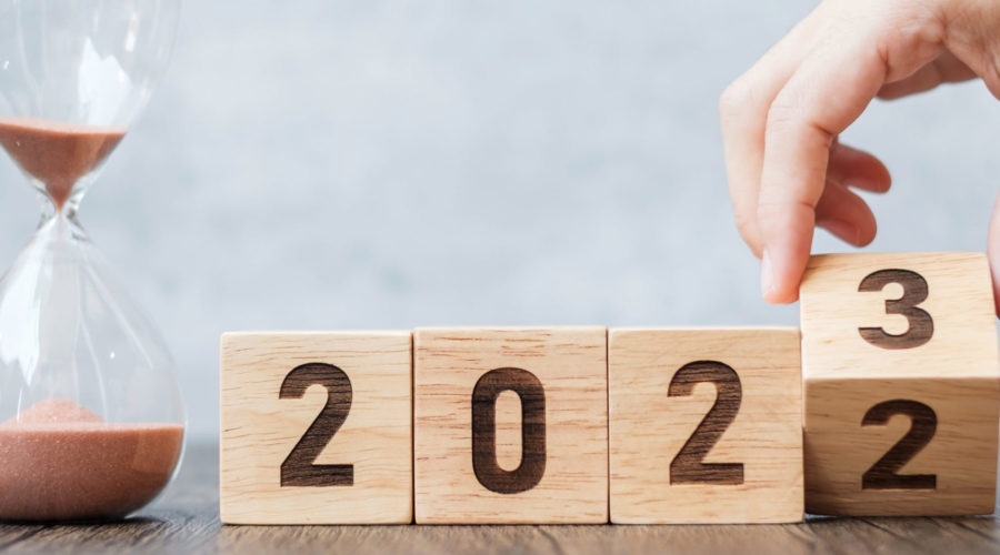 A hand flipping a wooden block from 2022 to 2023 next to an hourglass-it support